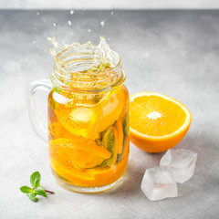Cold tea with orange, mint and ice, sweet summer drink, refreshing lemonade, juicy cocktail. Spray, splash