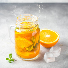 Cold tea with orange, mint and ice, sweet summer drink, refreshing lemonade, juicy cocktail. Spray, splash