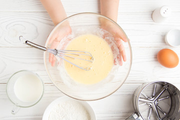 Children's small hands beat the dough for pancakes cooking in the kitchen