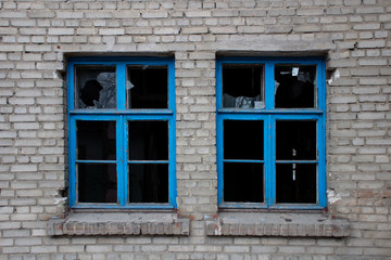 Blue frames of broken windows of an old, abandoned brick building.