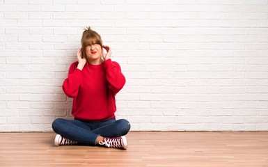 Redhead woman siting on the floor frustrated and covering ears with hands