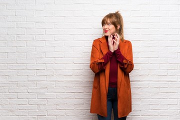 Woman with coat over white brick wall scheming something