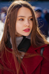 Closeup portrait of a young girl in a burgundy cashmere coat in the street