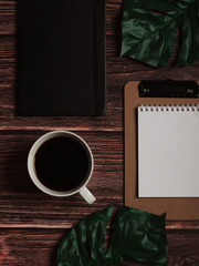 Black coffee, notebook, blank paper and monstera leaf on wooden desk background. Office concept. Flat lay. Top view. Copy space © oprzybysz