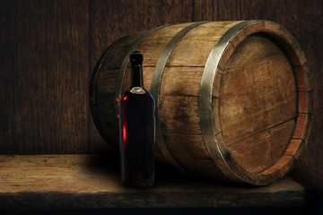 Red wine bottle on a old oak wooden table background barrel.