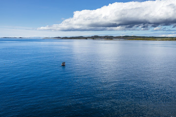 A small fishing boat near Western Norway coastline in a bright sunny day during summer season