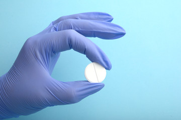 Close up of female doctor's hand in blue sterilized surgical glove holding white pill against blue background