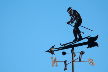 Skier weather vane against blue sky. Copy space for text message or promotional content.