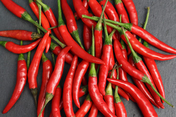 A lot of sharp hot spice red chilli cayenne pepper with wet drops of freshness water dew on a black graphite slate stone surface. Natural vegeterian diet organic vegetable. Dark food foto