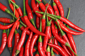 A lot of sharp hot spice red chilli cayenne pepper with wet drops of freshness water dew on a black graphite slate stone surface. Natural vegeterian diet organic vegetable. Dark food foto