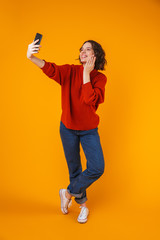 Excited emotional young pretty woman posing isolated over yellow wall background take selfie by mobile phone.