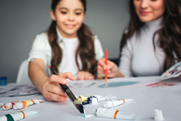 Beautiful brunette caucasian mother and daughter paint together in room. Cut view and blurred...