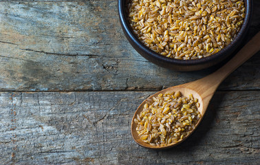 Dry bulgur wheat grains in wooden scoop or shovel, rustic style. Heap of uncooked siyez (black) bulghur cereal in bowl