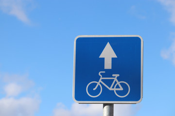 Bicycle road sign isolated on blue sky. White bicycle symbol on the blue square with arrow, the bike lane
