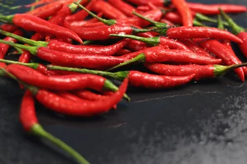 Fotobehang A lot of sharp hot spice red chilli cayenne pepper with wet drops of freshness water dew on a black graphite slate stone surface. Natural vegeterian diet organic vegetable. Dark food foto © Наталия Чубакова