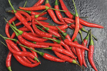 A lot of sharp hot spice red chilli cayenne pepper with wet drops of freshness water dew on a black graphite slate stone surface. Natural vegeterian diet organic vegetable. Dark food foto