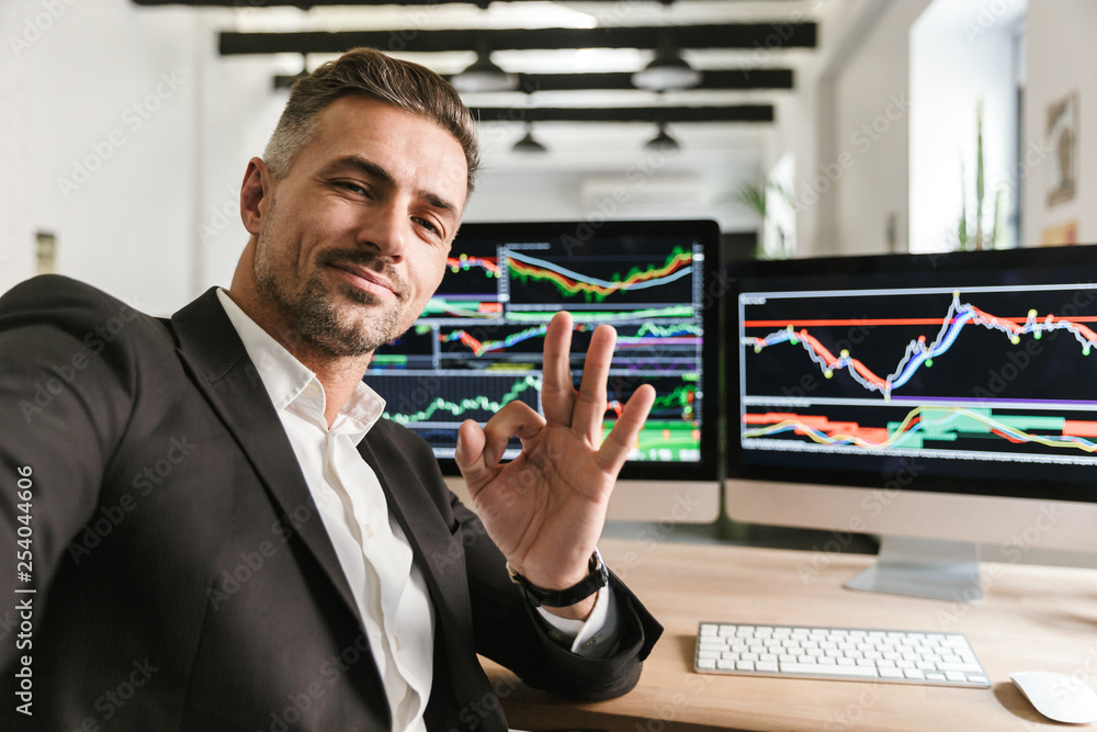 Poster photo of caucasian man taking selfie while working in office on computer with graphics and charts at