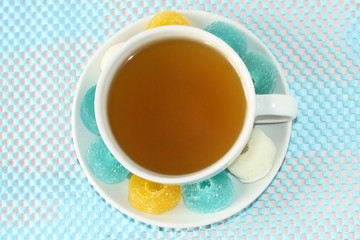 White cup with green tea on a saucer with multi-colored marmalade sweets. Sugar sweet Christmas sweets. Gelatinous sweet fruit candies for children.  Sweets and pleasures.