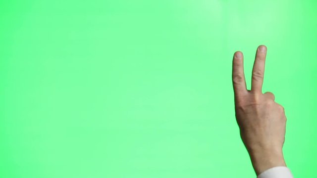 A man's hand doing a peace or victory gesture on a green screen background.