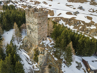 Aerial view of medieval tower ruins of fortess in forest. Stone tower on peak in Swiss alps with snow covered ground.
