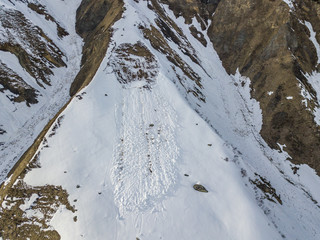 Aerial view of snow avalanche on mountain slope. Wet snow in spring sliding downhill.