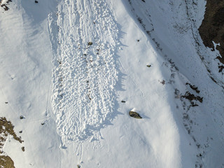 Aerial view of snow avalanche on mountain slope. Wet snow in spring sliding downhill.