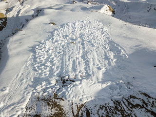 Aerial view of snow avalanche on mountain slope. Wet snow in spring sliding downhill.