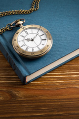 Vintage pocket watch clock with book on wooden background