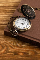Vintage pocket watch clock with book on wooden background
