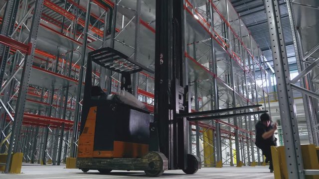 Two guys jump over a reach truck in an empty logistic center. Wide view
