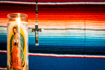 wood and silver crucifix with Virgin Mary prayer candle to the left, with Mexican blanket as backdrop.