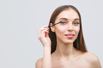 Young woman applying the black mascara on white