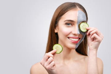 Woman with facial mask and cucumber slices in her hands on white background