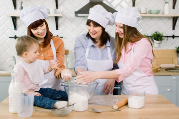 Little beautiful baby girl with mother, aunt and grandmother holding flour in their hands and...