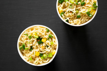 Tasty instant ramen noodles with beef flavoring in paper cups over black background. Flat lay, from above, overhead. Close-up.