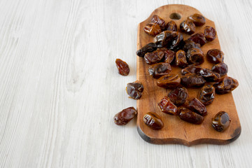 Dried dates on rustic wooden board over white wooden background, side view. Copy space.