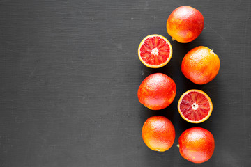 Whole and halved blood oranges on black background, top view. Flat lay, overhead, from above. Copy...