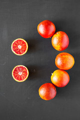 Whole and halved blood oranges on  black background, top view. Flat lay, overhead, from above.