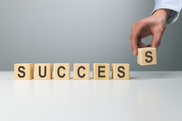 Woman's hand adjusting 'success' word made of wooden blocks. Success word from wooden blocks on desk. Business success