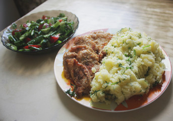 Dish consisting of fried meat and boiled potatoes and cucumber salad with green onions and tomatoes.