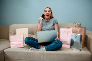 Online shopping at home. Young surprised woman with credit card is ready to Singles day on a sofa...