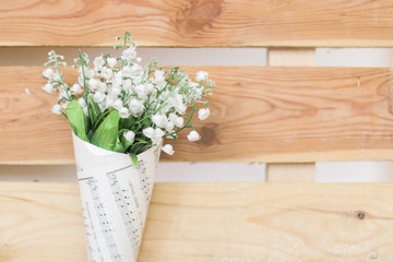 bouquet of small white flowers in a sheet of music on a wooden background