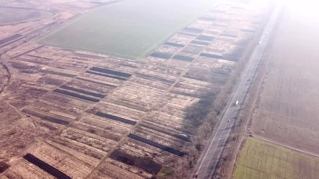 Aerial drone view of a highway road with moving cars between gray fields.