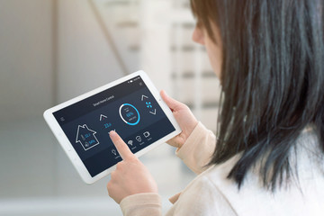 Woman control temperature in living room with smart home control app on tablet. View from the...