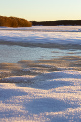 Snow and ice covered lake, with reed lit up by the setting sun that creates a warm light.