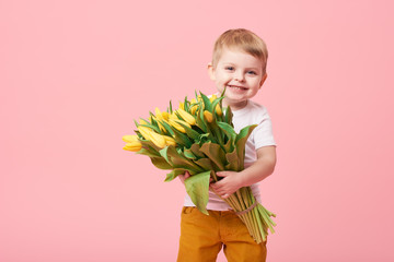 Adorable smiling child with spring flower bouquet looking at camera isolated on pink. Little...