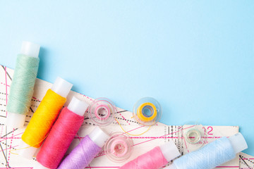 Multicolored thread coils and measuring tape on blue background. Sewing supplies, pattern and...