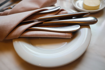 Table setting in the restaurant. White plate with  cutlery in napkin on a marble background