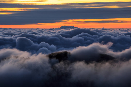 Abstract photograph above the clouds, sea of clouds effect, flying through the sky, aerial view, puffy clouds, orange sunset sky. Low pressure front atmospheric effect, cloudscape, clear weather.