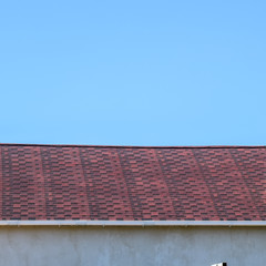 Fototapeta na wymiar Roof from multi-colored bituminous shingles. Patterned bitumen shingles. Bituminous burgundy roof.